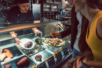 Experienced chef choosing raw seafood from the freezer for two customers in a trendy restaurant or cafeteria with fresh food
