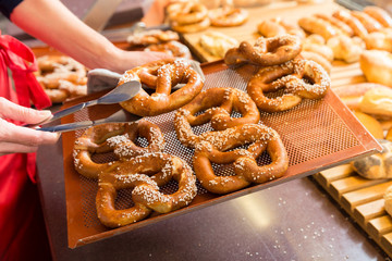 Sales lady in bakery shop selling pretzels and bread from the display 