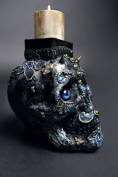 Skull decorated with colorful stones with candle on black background
