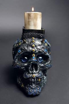 Skull decorated with colorful stones with candle on black background