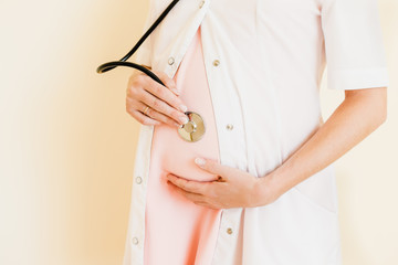A pregnant doctor listens to herself belly with a stethoscope.