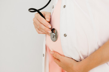 A pregnant doctor listens to herself belly with a stethoscope.