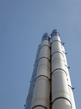 a group of tall modern steel industrial chimneys standing against a bright blue sky and white clouds