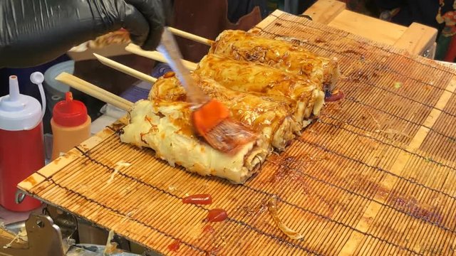 Process of cooking okonomiyaki roll on traditional bamboo mats. Japanese pizza