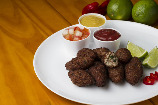Traditional arabic food, kibes served on white plate accompanied by salad, ketchup, mustard and lemon on yellow wooden table