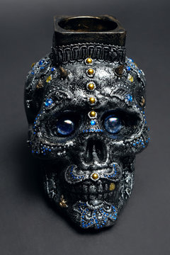 Skull decorated with colorful stones with candle on black background