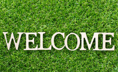 Wood alphabet in word welcome on artificial green grass background © bankrx