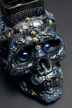 Skull decorated with colorful stones with candle on black background