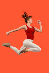 Fototapeta na wymiar Freedom in moving. Pretty young woman jumping against orange background