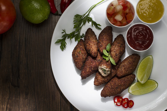 Traditional arabic food, kibes served on white plate, accompanied by salad, ketchup, mustard, pepper and lemon on rustic wooden table