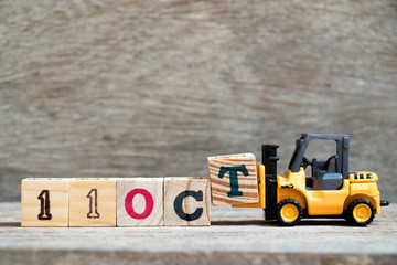 Toy forklift hold block T to complete word 11 oct on wood background (Concept for calendar date in month October)
