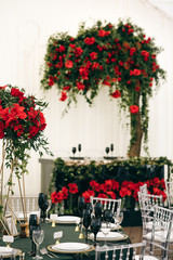Fototapeta na wymiar Tall bouquets of roses stand on dark green tables in restaurant hall