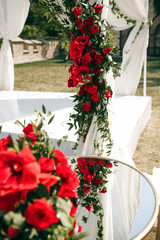 Fototapeta na wymiar Red flowers and greenery decorate white wedding altar and little table before it