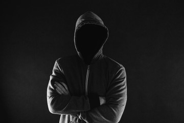 Fototapeta na wymiar Anonymous and faceless man under hoodie with arms crossed isolated over dark background - incognito and mysterious criminal on internet activities concept.