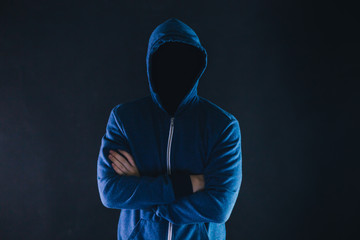 Anonymous and faceless man under hoodie with arms crossed isolated over dark background - incognito...