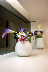 Beautiful purple flowers in white vase on white shelf for room decoration.