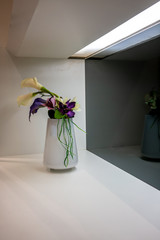 Beautiful purple flowers in white vase on white shelf for room decoration.