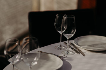 Banquet and celebration concept. Served table for special occasion with empty plates, wine glasses, forks and knives on white tableclothes in cozy restaurant