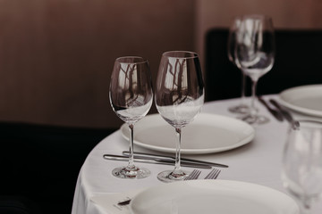 Elegant served table with glasses, dishes on white tableclothes. Banquet facilities. No people at table. Holiday eve. Shot of decorated table for party in restaurant