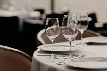 Shot of banquet table setting against restaurant interior. Cafe set. Empty wine glasses, plates, knives and forks. Served table for dinner. No people on photo