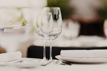 Wedding table set for banquet. Glasses and plates served on table. Dinner setting. Luxury cutlery. Festive event. Horizontal shot. Blurred background.