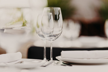 Fototapeta premium Wedding table set for banquet. Glasses and plates served on table. Dinner setting. Luxury cutlery. Festive event. Horizontal shot. Blurred background.