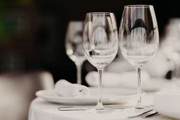 Indoor shot of empty glasses on festive dinner table with white tablecloth against dark blurred background. Wedding banquet. Wonderful decor