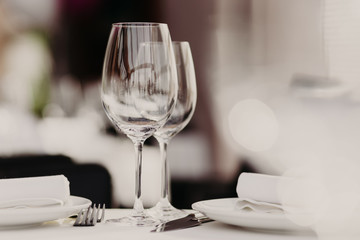 Empty glasses stand near plates and forks on banquet table decorated with white tablewear. Festively served table against blurred background in restaurant