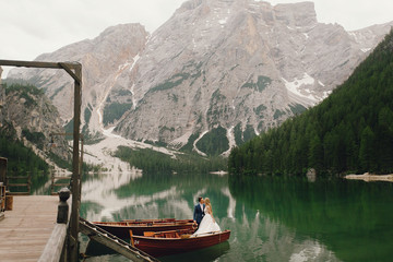 Fototapeta premium Bride and groom enjoy the moment standing in the boat somewhere in Italian Dolomites