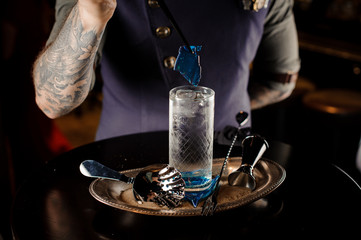 Bartender with tattoo making fresh and sweet summer cocktail with blue piece of caramel on the tray