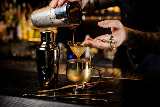 Bartender with tattoo pouring fresh and tasty summer drink into the copper mug