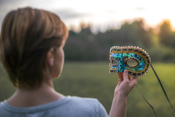 Woman holding a Venetian mask with her hand.