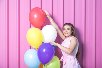 Fototapeta na wymiar Fashionable girl touching colorful balloons on rose metal wall