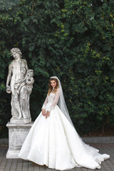 Fototapeta na wymiar Charming bride poses before old antique statue in the garden
