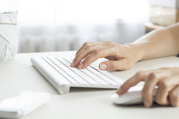 A woman uses a keyboard and a computer mouse sitting at the office table, in the workplace. 