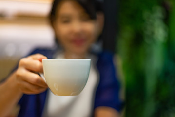 Blurred image of Asian woman holding white cup
