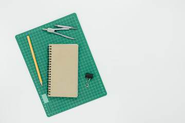 Table top view aerial image of back to school of education season background concept.Flat lay paper green rubber cut board with note nook and pencil on modern rustic white wooden.Free space for text.