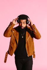 Stylish, handsome and cool African American man with beard, listening to music, isolated on pink studio background