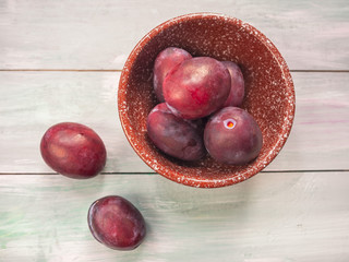 Ripe red plums in a ceramic bowl on a table.