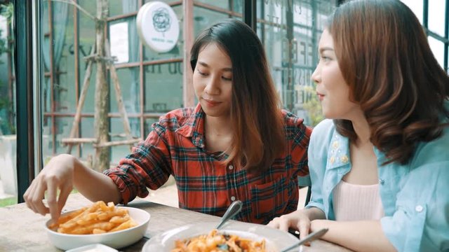 Beautiful happy Asian women lesbian lgbt couple sitting each side eating a plate of Italian seafood spaghetti and french fries at restaurant or cafe while smiling and looking at food.