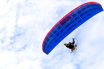 Motor paraglider flying in blue sky with white cloud in background.