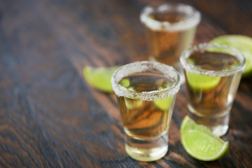 Three glasses of alcohol and lime slices in the defocus, on a dark wooden background