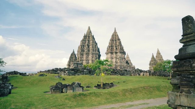 Prambanan temple and green lawn in Jogjakarta, Indonesia on cloudy day with some blue sky, slide left