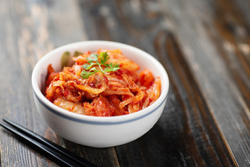 Kimchi cabbage in a bowl with chopsticks for eating on wooden background, Korean food