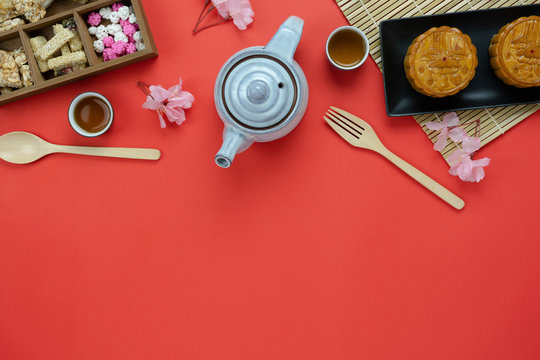 Table top view aerial image of decorations Chinese Moon Festival background concept.Flat lay meal set of coffee break the sweet cake & tea pot with snack on red paper backdrop.creative design mock up