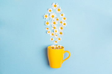 Yellow mug and chamomile flowers on a blue background. Chamomiles come out of the mug like steam.