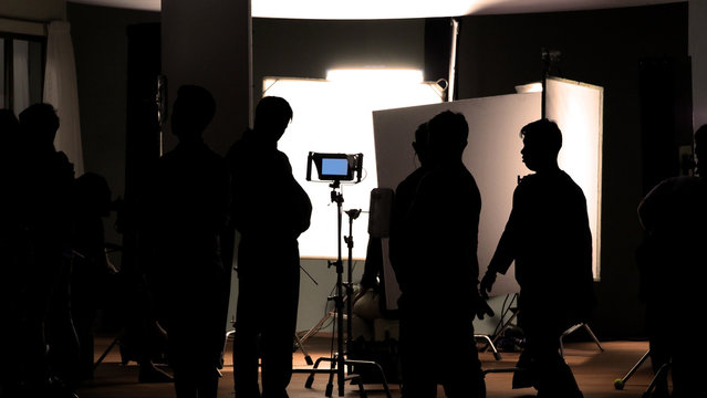 Video production behind the scenes which film crew team in silhouette shooting or recording tv movie commercial with professional equipment such as high definition 4k camera with monitor in studio set