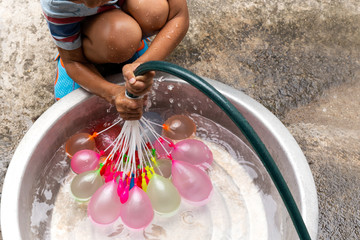 Little boy with water hose filling colorful water balloons in bucket.