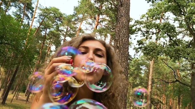 Attractive young woman blows soap bubbles in beautiful park in summer