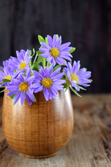Little violet asters in a wooden vase on a table